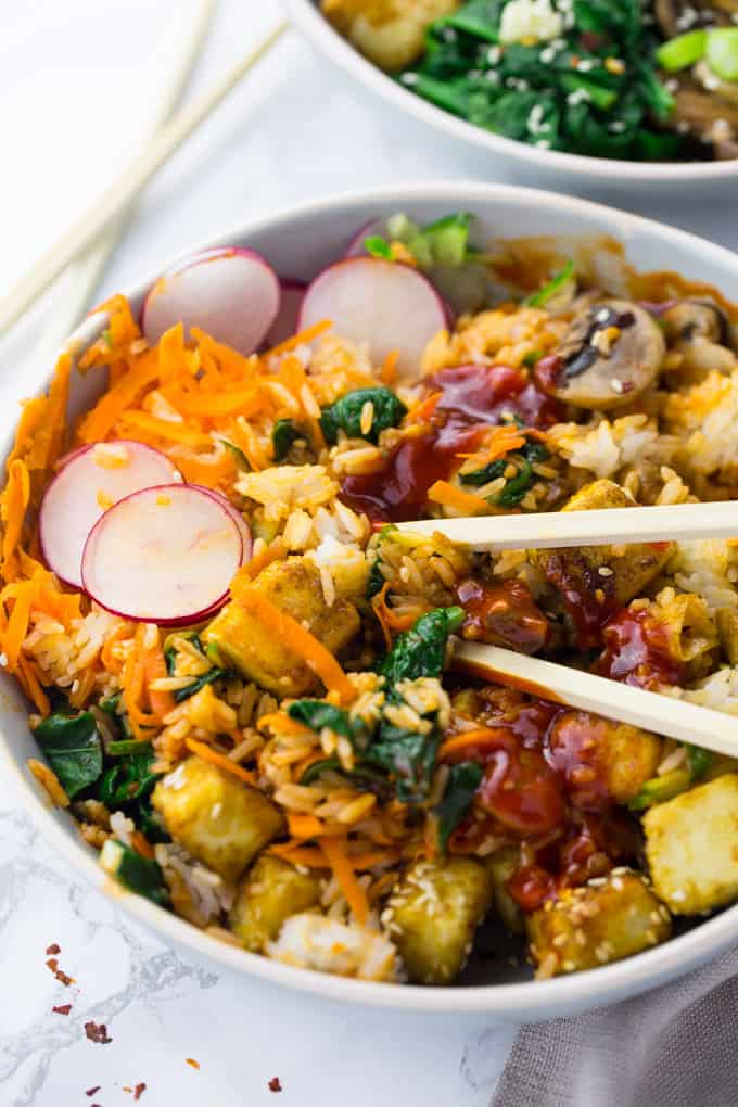 a grey bowl of Bibimbap with chop sticks on a marble countertop