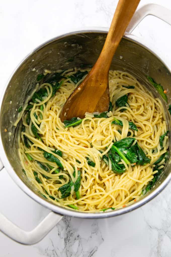 Lemon Spaghetti with Spinach in a pot with a wooden spoon on a marble countertop 