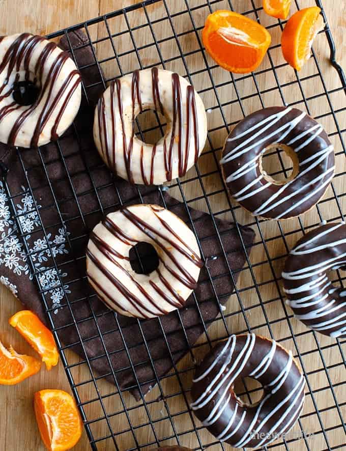 vegan orange donuts with chocolate glaze on a cooling rack with oranges on the side 