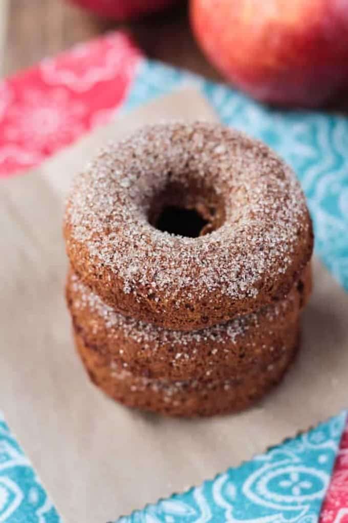 a stack of three vegan donuts topped with sugar and and apple in the background 