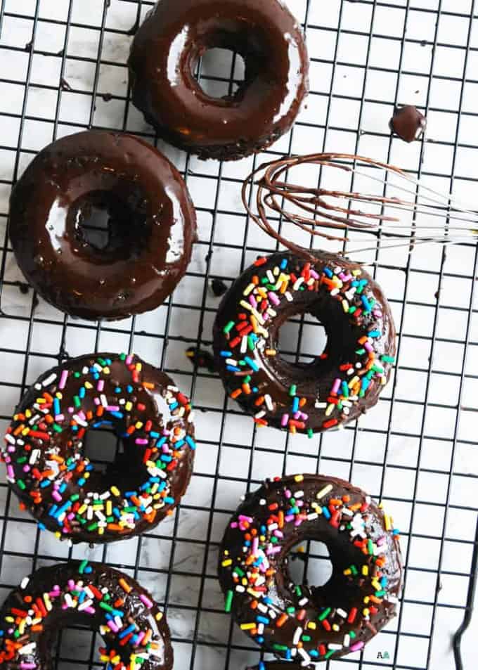 six vegan chocolate donuts on a cooling rack with a whisk on the side