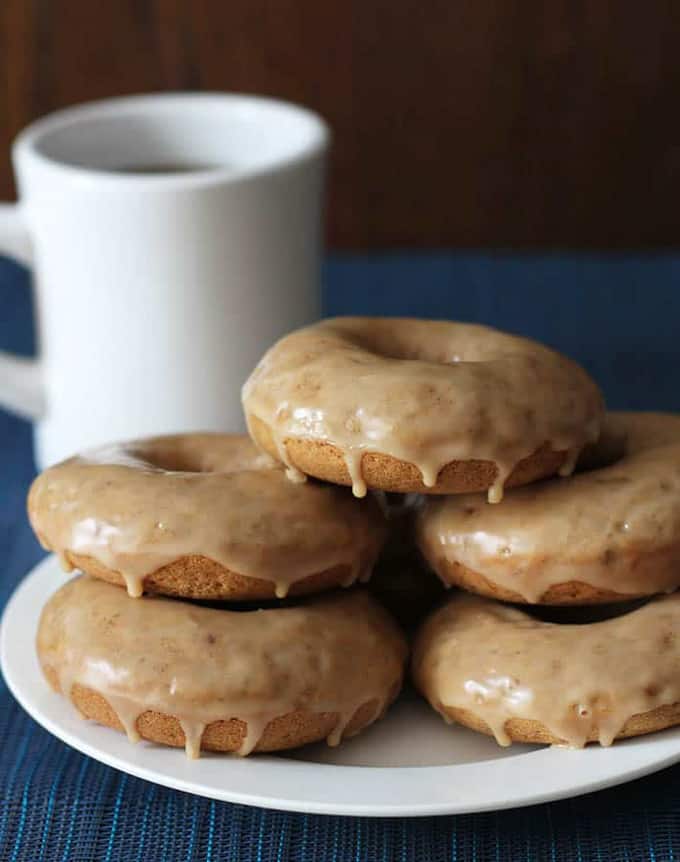 five vegan donuts on a white plate with a white mug in the background 