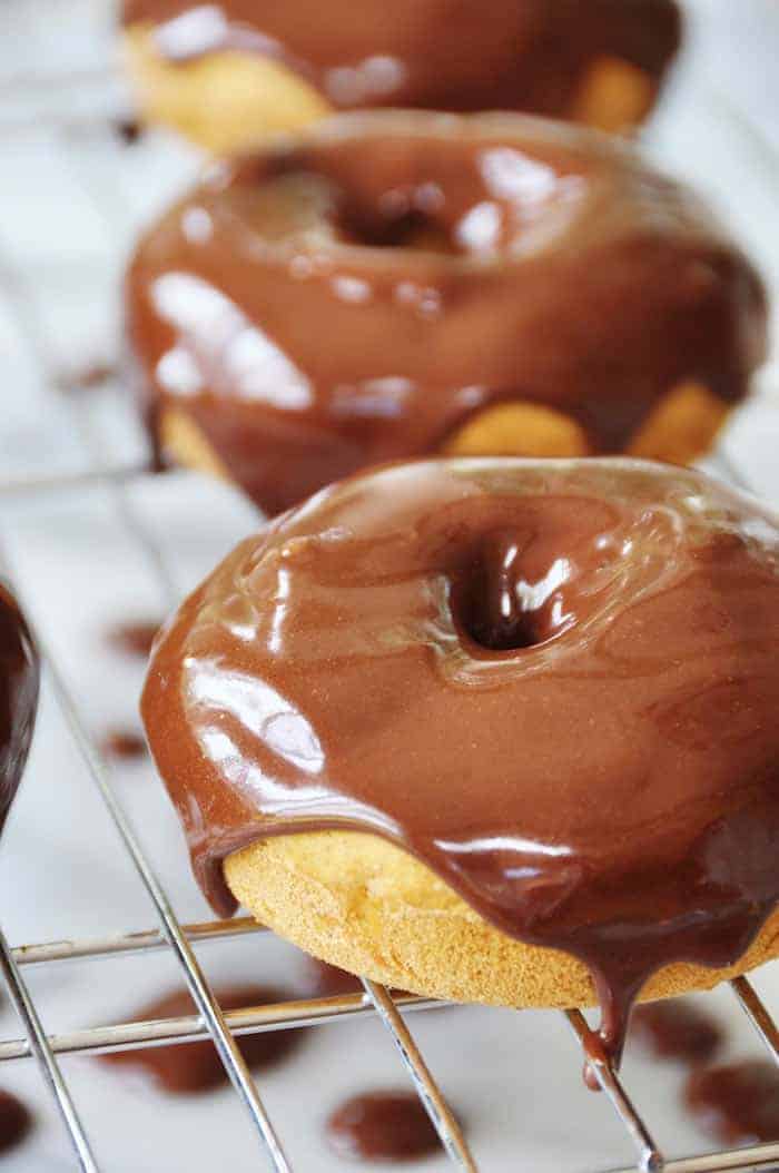 three vegan donuts with chocolate glaze on a cooling rack with dripping chocolate 