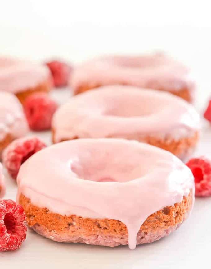 three vegan donuts on a white surface with raspberries on the side 