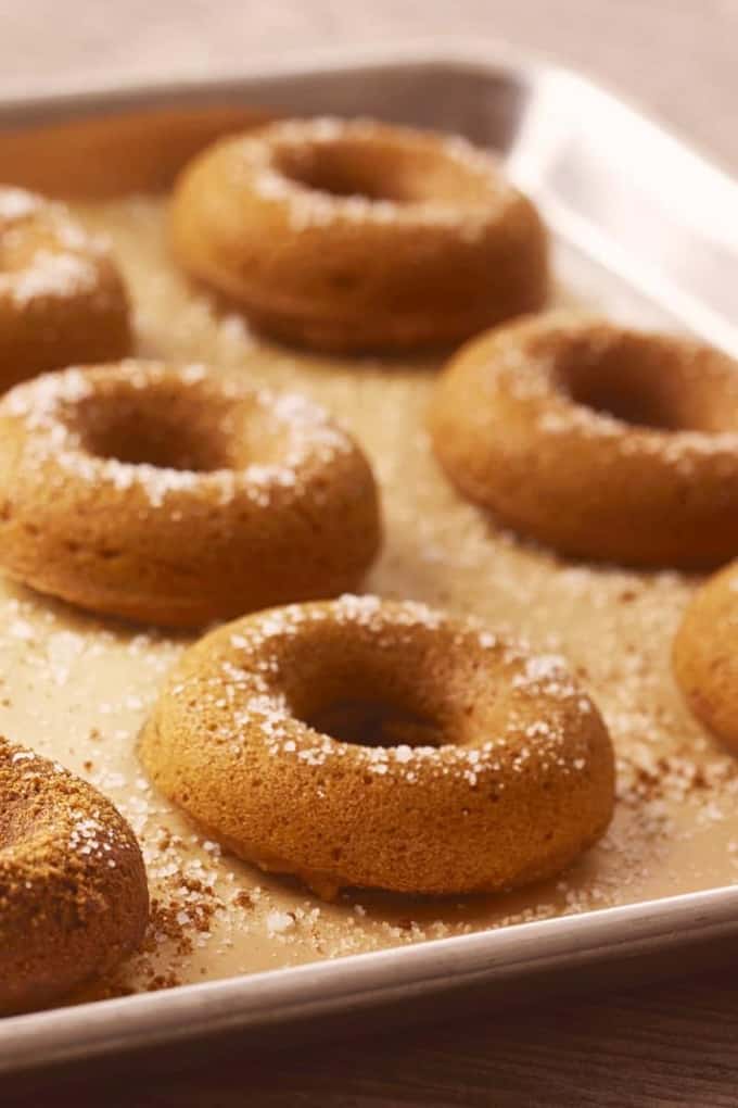 seven vegan pumpkin donuts on a baking tray 