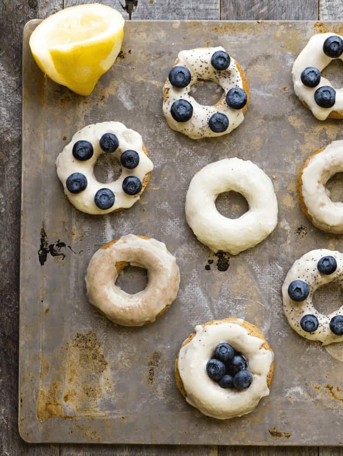 vegan lemon poppyseed donuts with blueberries on a baking tray with a lemon on the side 