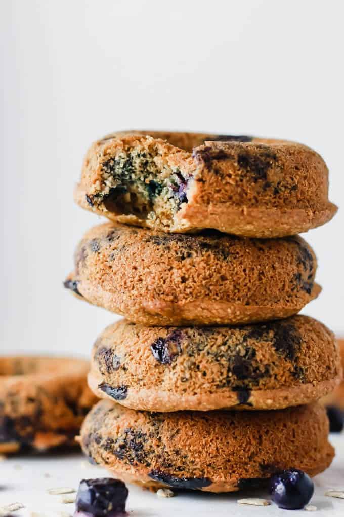 a stack of four vegan blueberry muffins with two blueberries on the side with a white background