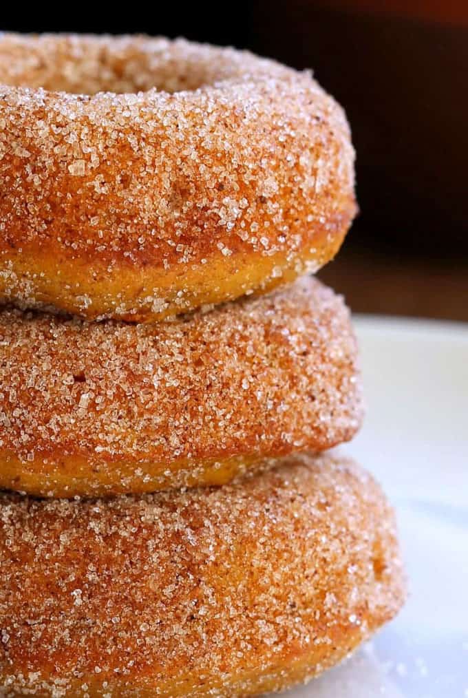 a stack of three vegan donuts with sugar on top and a black background