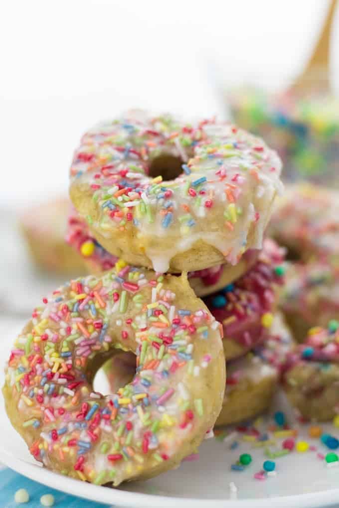 a stack of four vegan funfetti donuts on a white plate with another donut in front and a glass of funfetti in the background 