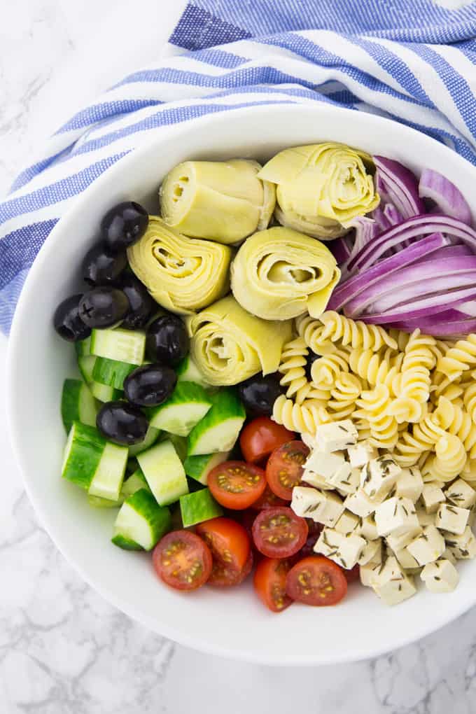 ingredients combined for the Greek pasta salad in a bowl without dressing in preparation of the salad