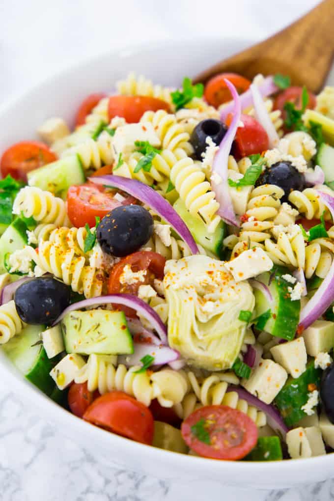 close-up of Greek pasta salad with red onions, olives, cucumber, artichokes, and tomatoes