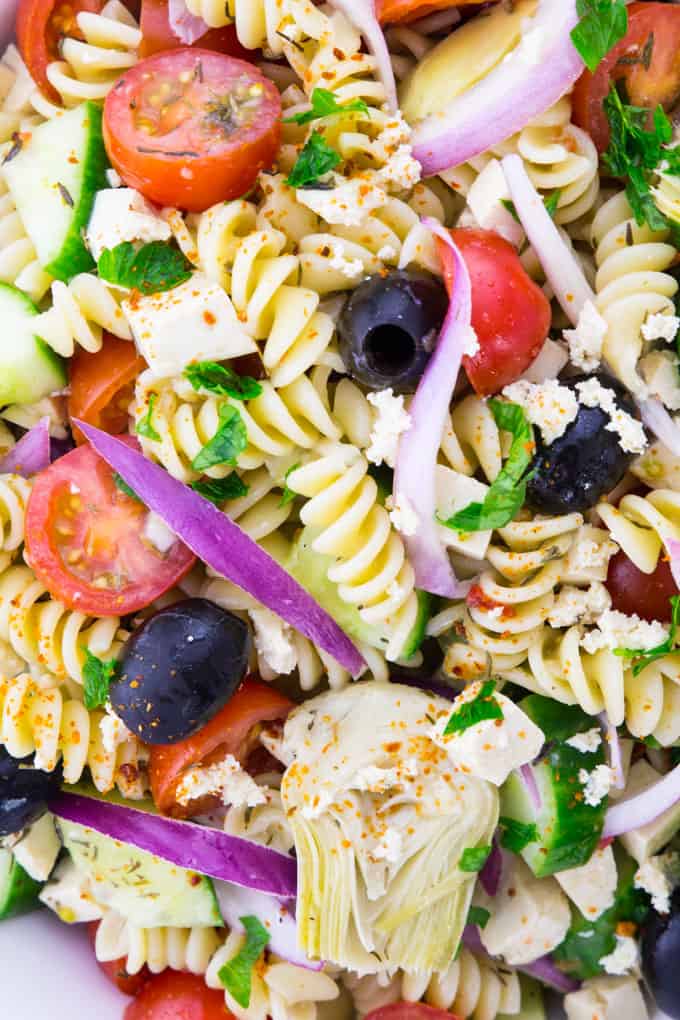 super close-up of Greek pasta salad with tomatoes, cucumber, red onions, artichokes, and black olives