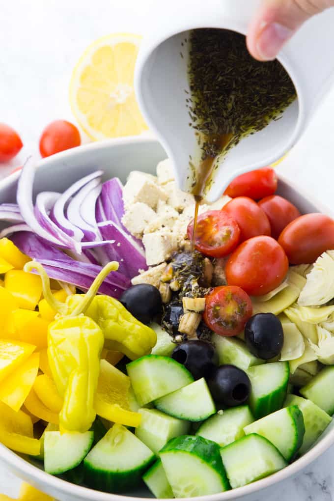 Preparation of the Greek pasta salad: the Greek vinaigrette with balsamic vinegar is poured over the chopped-up ingredients for the pasta salad