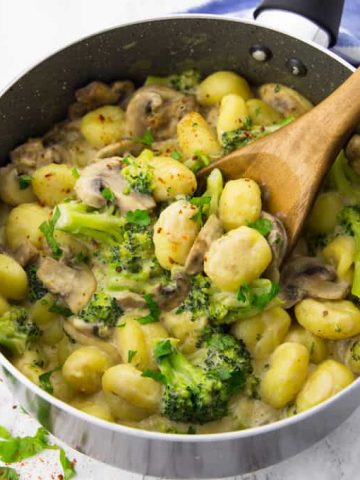 vegan gnocchi with mushrooms and broccoli in a pot with a wooden spoon