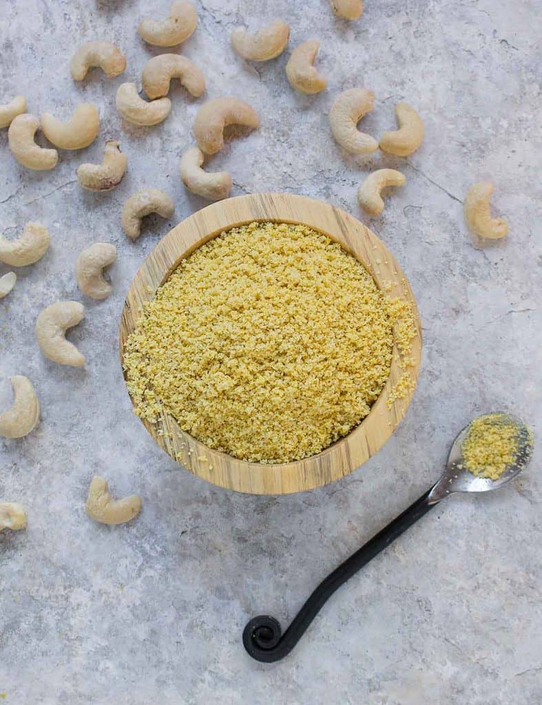 Vegan parmesan cheese in a wooden bowl with cashews on the side on a concrete counter top 