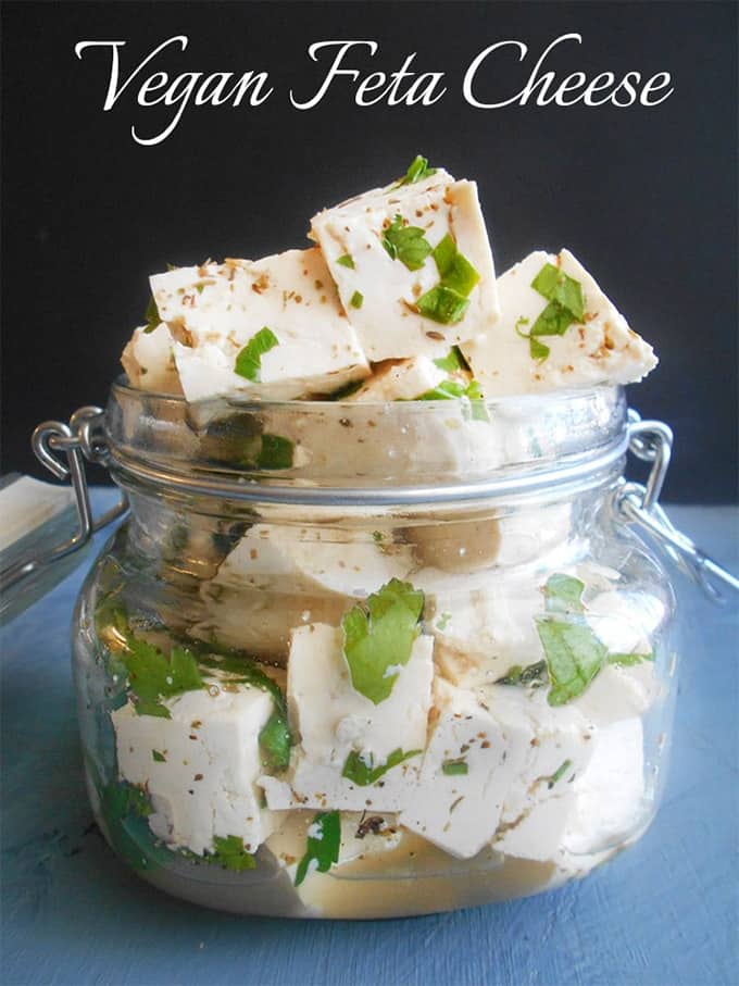 vegan feta cheese cubes in a glass jar with a black background and the writing "vegan feta cheese" 