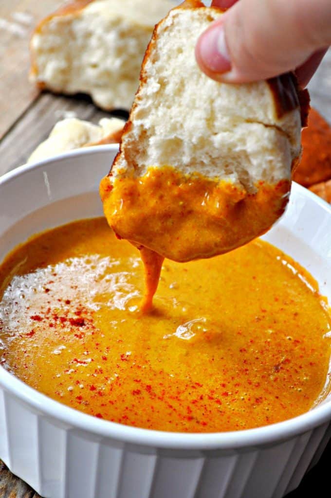 vegan beer cheese dip in a white bowl with a hand dipping a slice of bread into it 