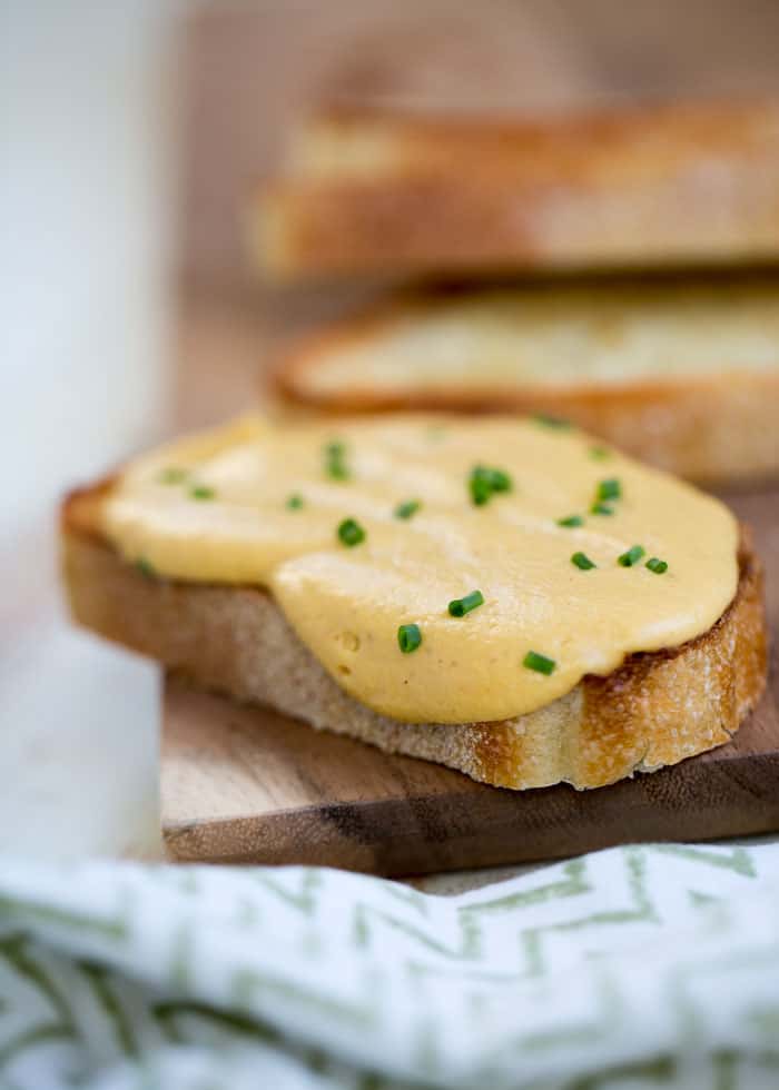 vegan cheese sauce on roasted bread on a wooden board with chives sprinkled on top 