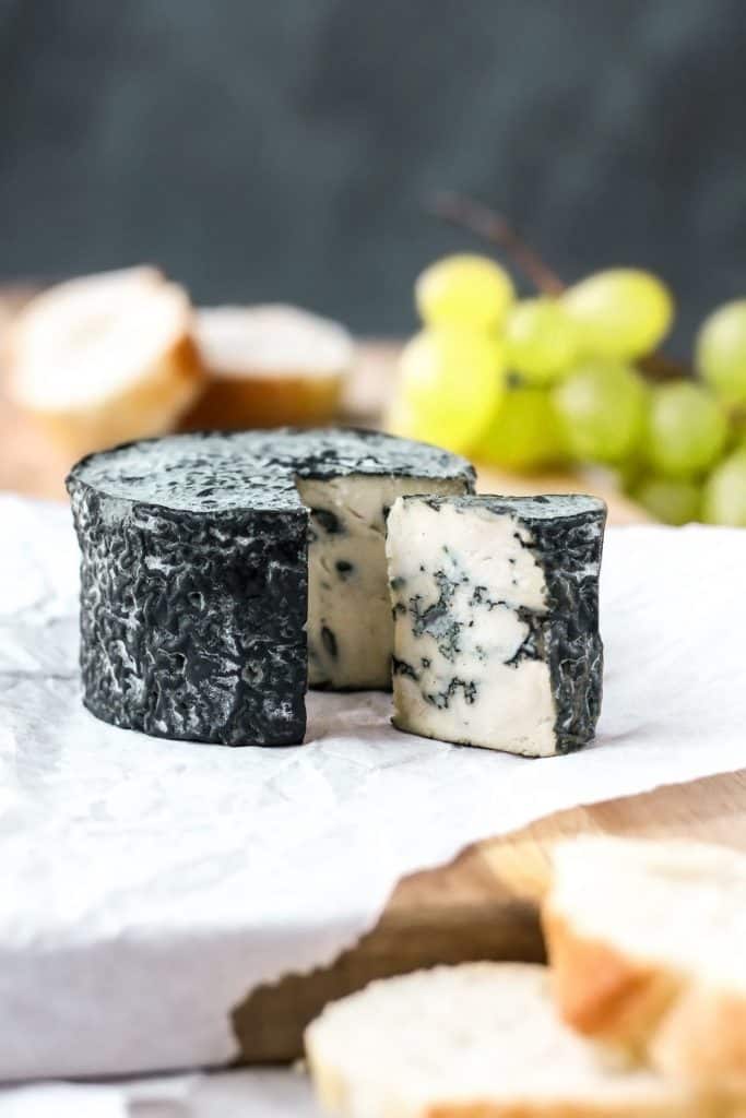 vegan blue cheese on a wooden board with grapes and a few pieces of baguette in the background 