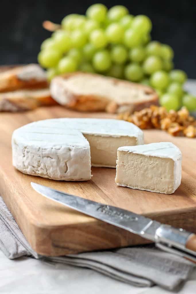 Vegan Camembert cheese on a wooden board with grapes and bread in the background 