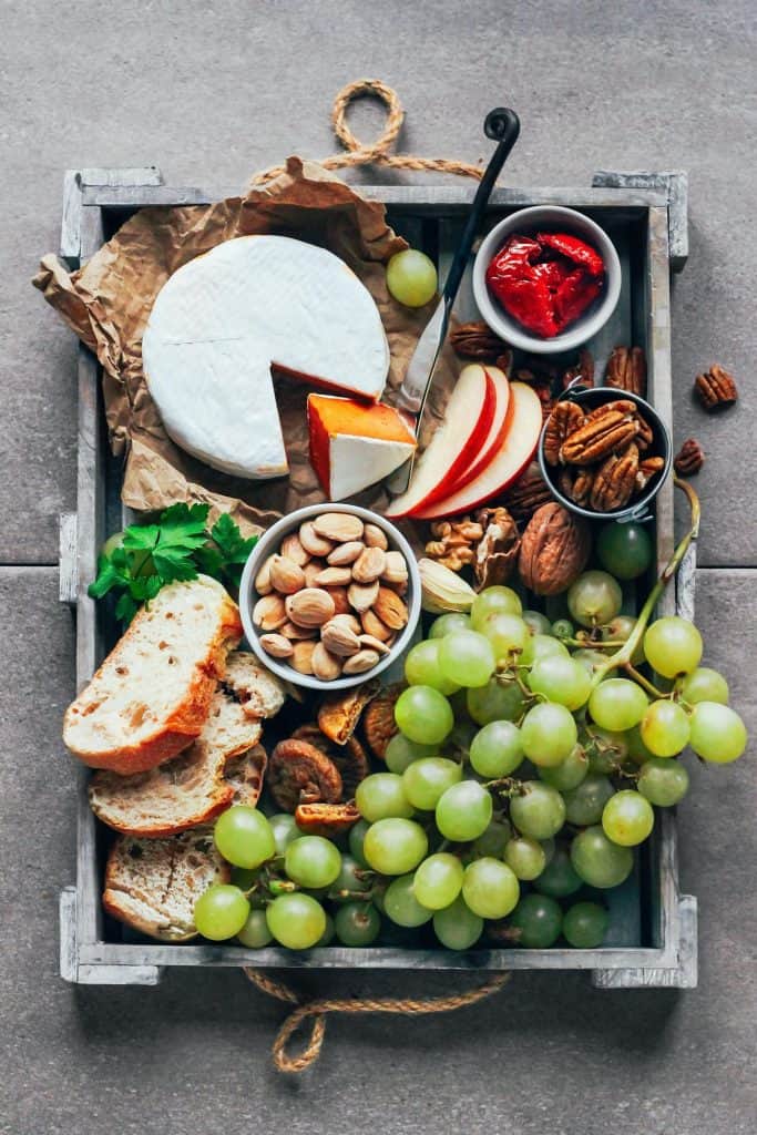 Vegan sun-dried tomato camembert in a wooden tray with nuts, bread, apple slices, and crapes 