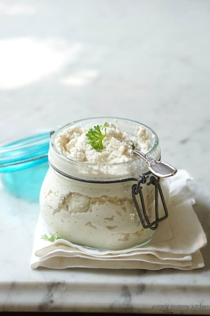 vegan ricotta cheese in a wooden jar with a spoon on a marble counter top 