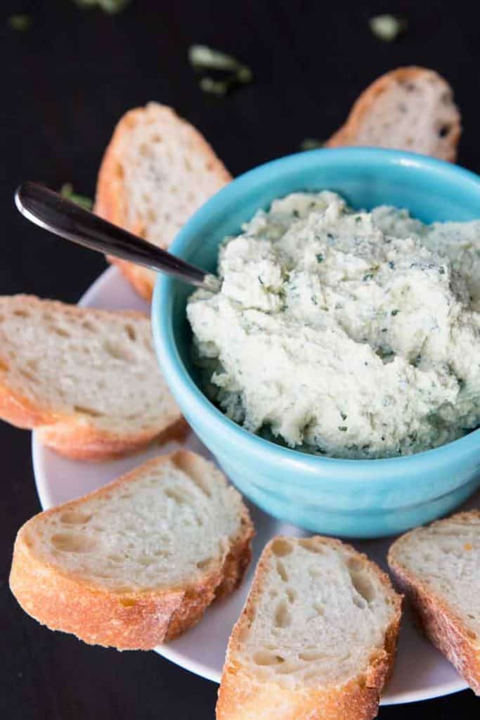 Vegan ricotta cheese in a blue bowl with a spoon and slices of bread on the side 