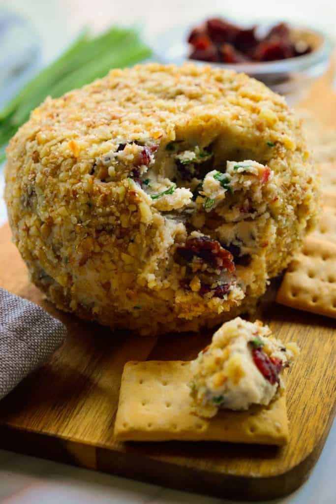 a vegan rosemary cranberry cheeseball on a wooden board with crackers on the side 