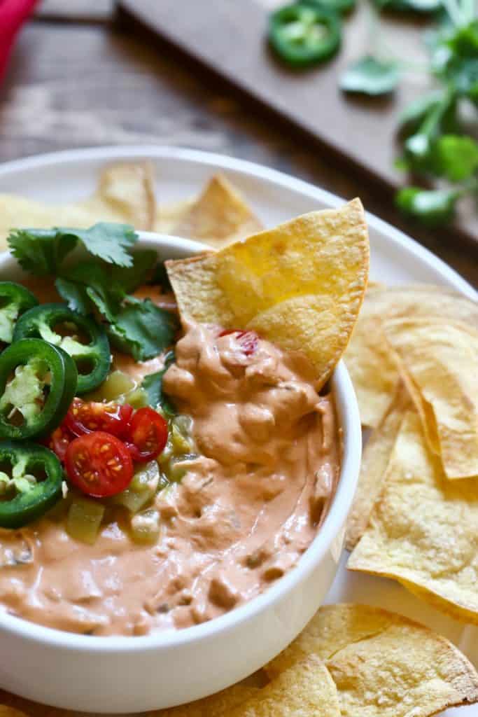 vegan queso in a white bowl with green chilis and fresh cilantro on top and nachos on the side 