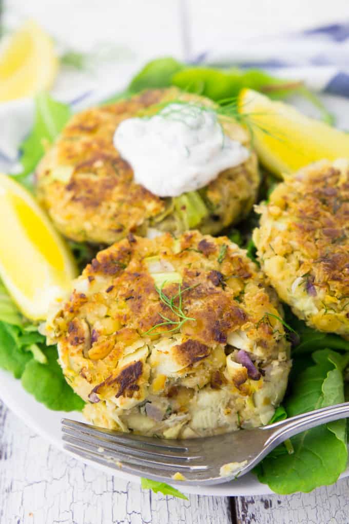 three vegan crab cakes on a bed of salad with lemon wedges on the side