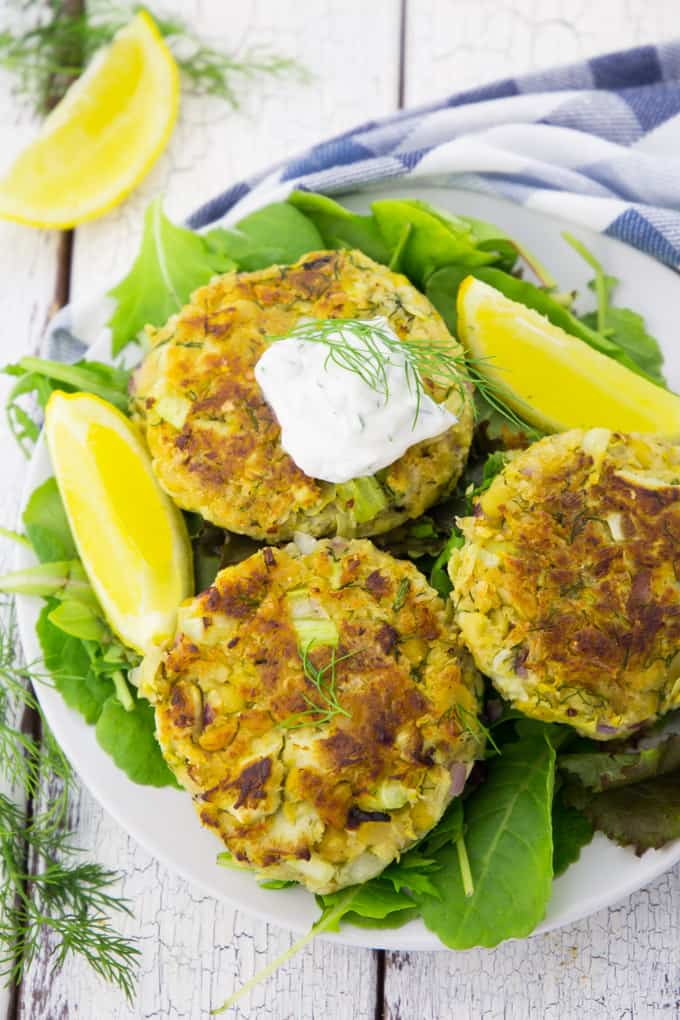 three vegan crab cakes on a white plate on a wooden countertop 