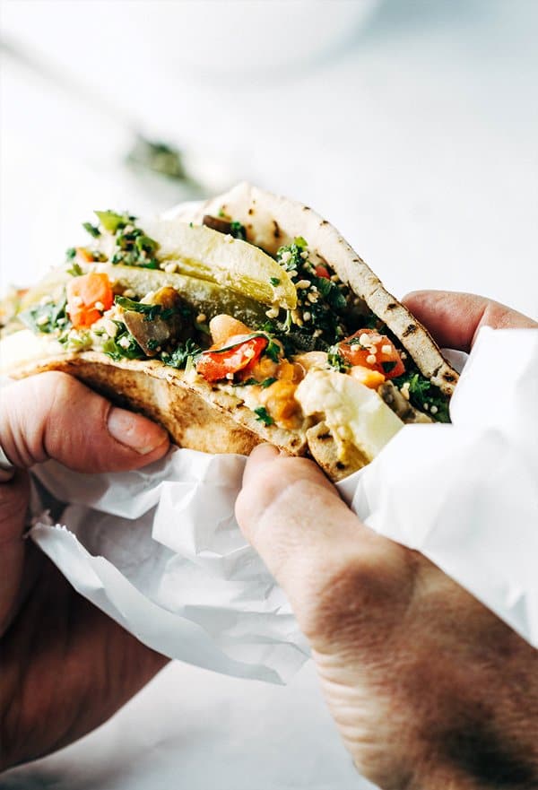 Two hands holding a sabich sandwich