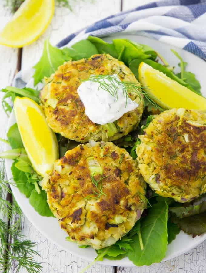 Three vegan crab cakes on a plate with lemon slices 