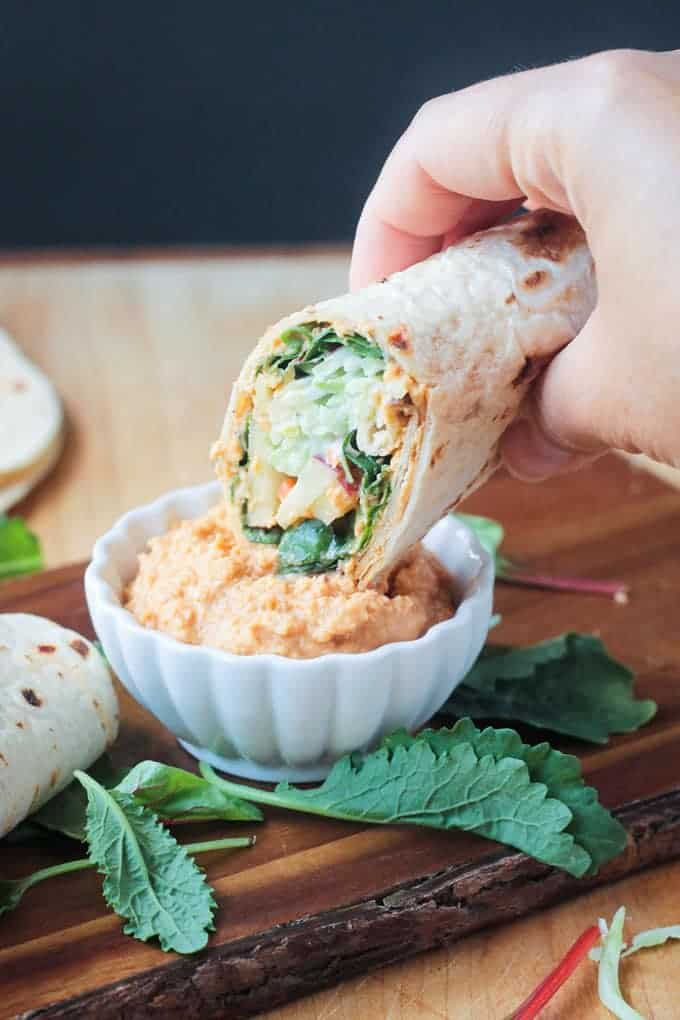 Broccoli Slaw Veggie Wrap Being Dipped Into Spicy Hummus 