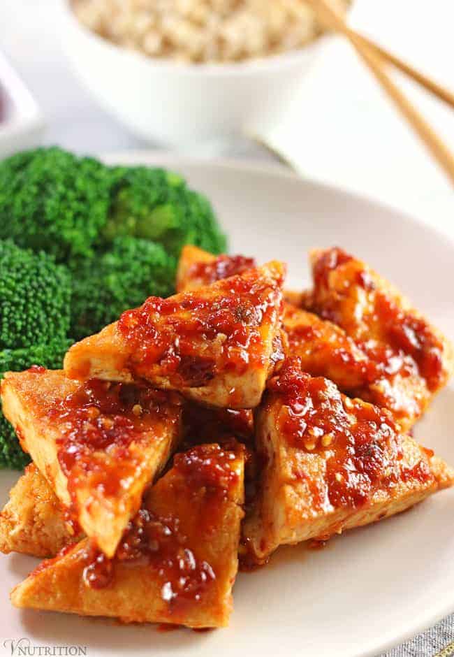Tofu in Chili Garlic Sauce with Broccoli on a Plate with Chop Sticks and Rice in the Back