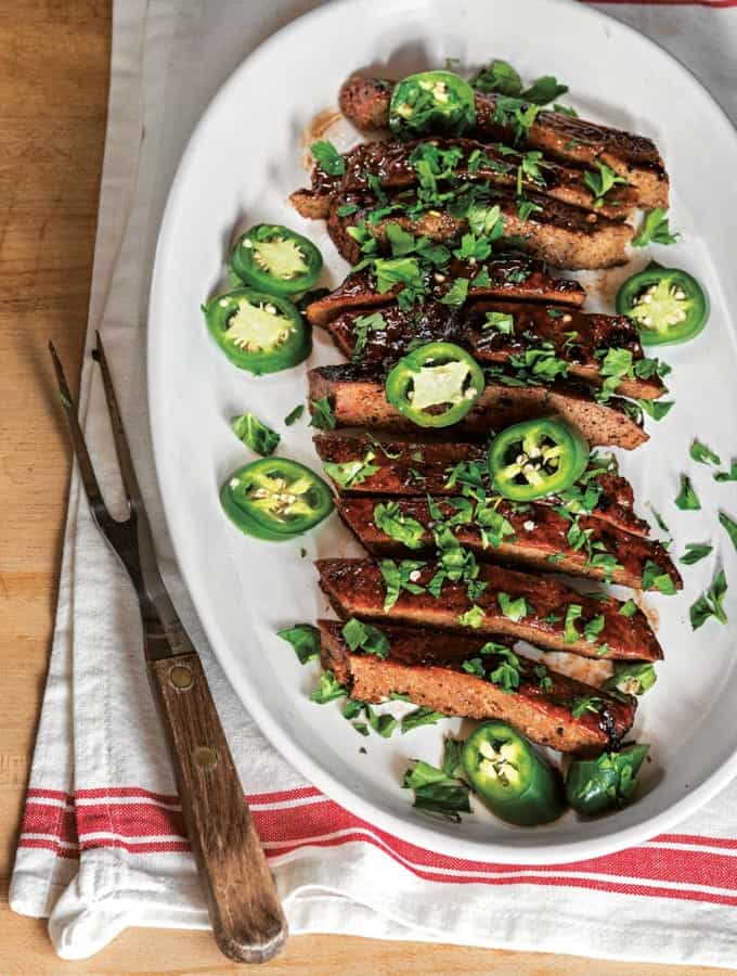 Vegan ribs on a plate with jalapeno peppers on top and barbecue tongs on the side