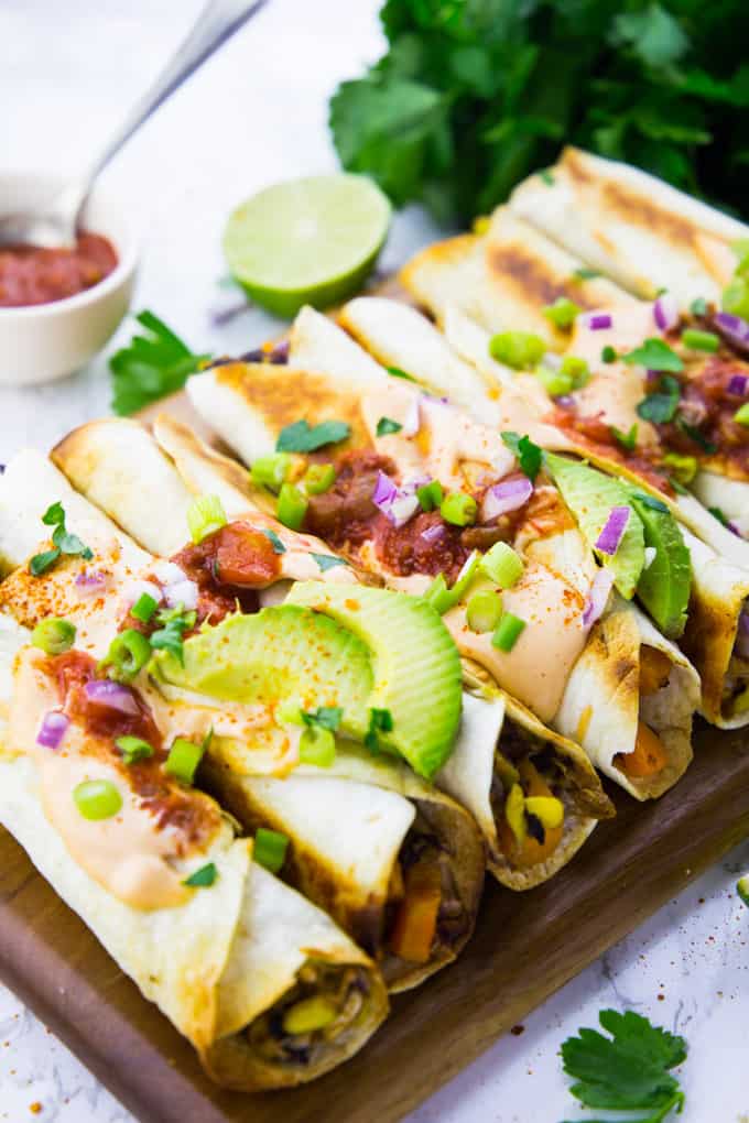 taquitos with avocado slices, chipotle sauce, and red onions on top