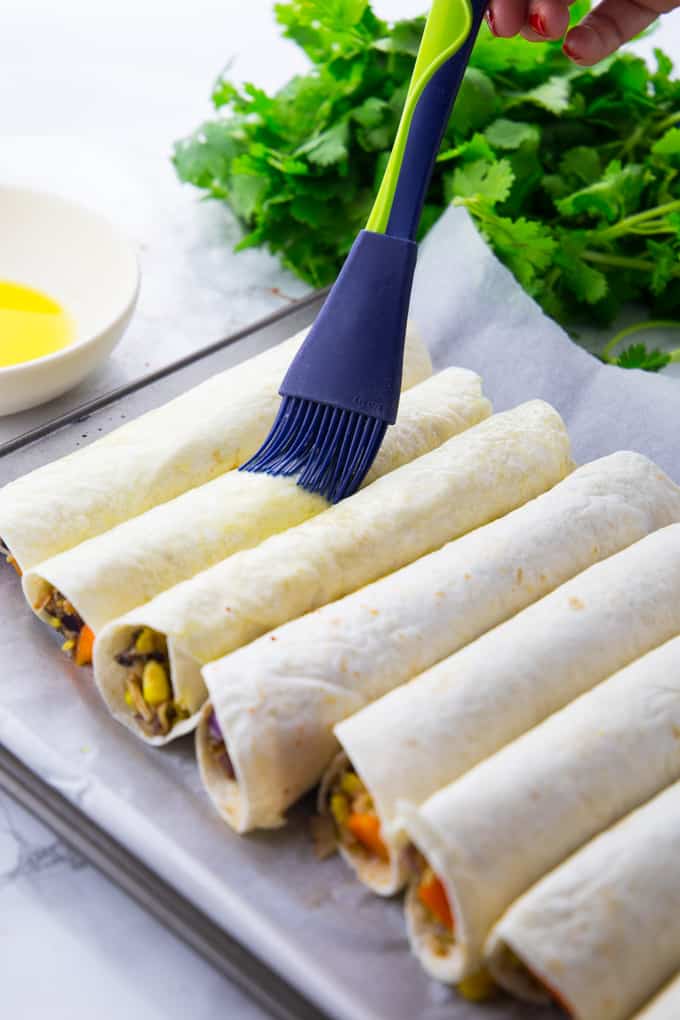 taquitos on baking sheet are brushed with olive oil