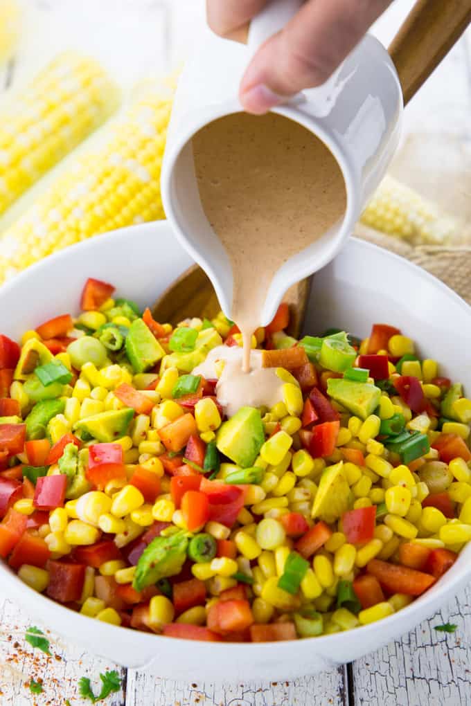 Chipotle mayonnaise dressing is being poured over corn salad in a bowl