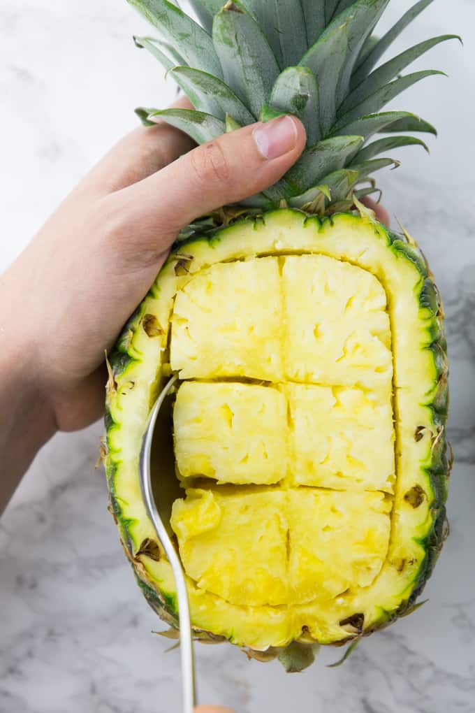 A Hand Spooning Pineapple Pieces out of a Pineapple to Make a Pineapple Bowl