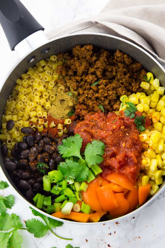 Uncooked pasta, corn, black beans, bell pepper, and veggie crumbles in a pot