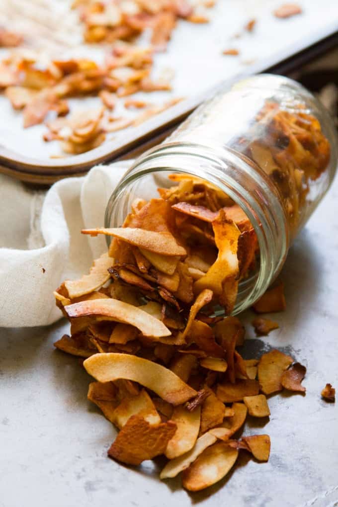 A jar of freshly baked coconut bacon with a baking sheet in the background 
