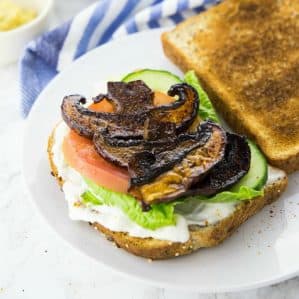 en sandwich med salat, tomater og bacon med svampe på en hvid tallerken