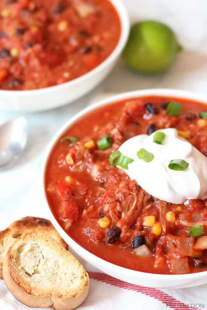 a bowl of jackfruit chili with on a white counter top with another bowl in the background and a slice of toasted bread on the side