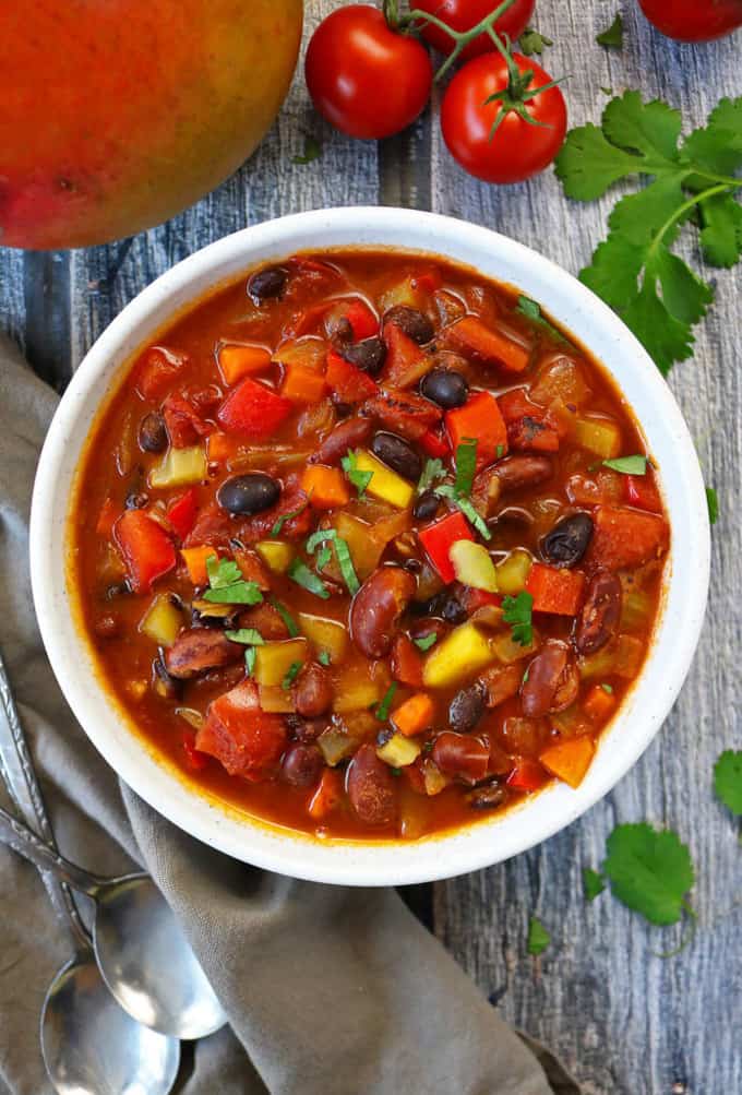 Easy Vegetarian Mango Chili in a white bowl with a mango, cherry tomatoes, and cilantro on the side