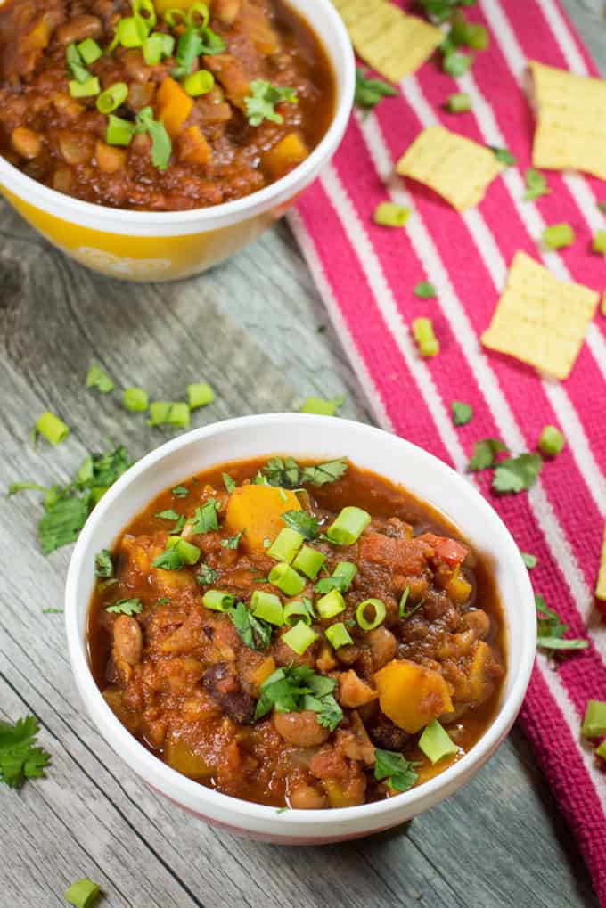 Two Bowls of Slow Cooker Vegan Chili on a Wooden Counter Top with a Pink Napkin on the Side 