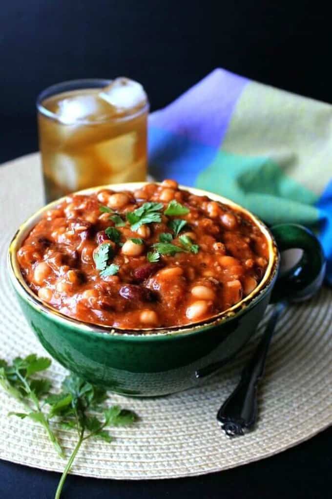 vegan chili in a green bowl on a black surface with a glass and a blue napkin in the background