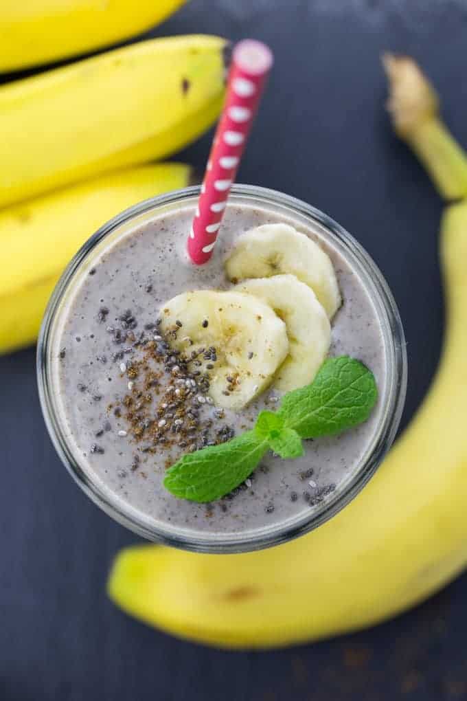 A glass of banana smoothie with a red straw and chia seeds on top on a black counter top