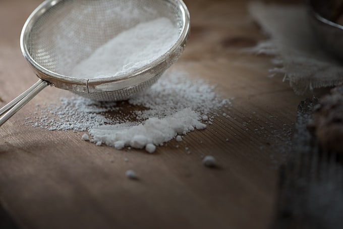powdered sugar in a sieve on a wooden counter top