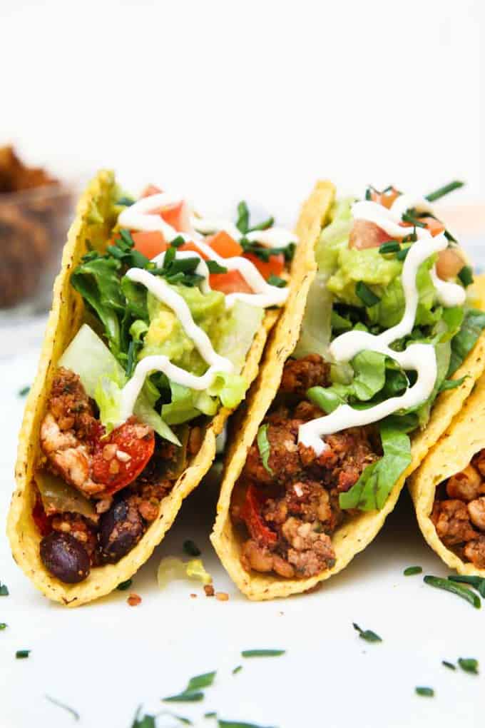 Three Black Bean Tofu Tacos with Walnut Crumble on a White Surface with Sprinkled Chopped Herbs